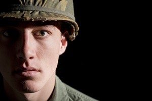 Close up portrait of a young American soldier from the Vietnam War period. Spot lit face against a black background.